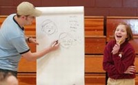 Maggie Wieczorek laughs at the cartoon drawing of her as cartoonist Jason Kotecki illustrates how to show emotion at Peru Catholic School recently. Kotecki, who attended Peru Catholic, returned to the school to show students his art. (Photo by Kemp Smith)